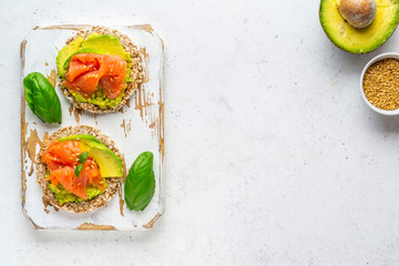 Open face sandwiches on buckwheat crispbread toast with avocado, salmon, basil, flax seeds served on wooden rustic board.