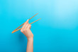 Girl's hand showing chopsticks on blue background. Asian cuisine concept with empty space for your design