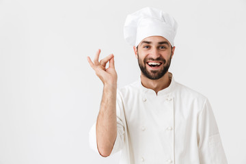 Wall Mural - Cheerful pleased young chef posing isolated over white wall background in uniform.