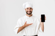 © Drobot Dean - Positive smiling young chef posing isolated over white wall background in uniform holding mobile phone showing empty display.