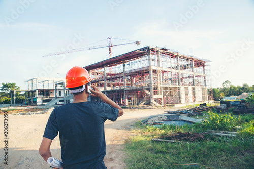 Construction Engineer And Safety Health Officer Concept Young Man Engineer Wear Safety Hat Helmet Safety Officer Inspector And Holding Blue Print Talking On Smartphone In Front Of Construction Sit Buy This Stock Photo