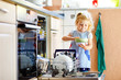 © Irina Schmidt - Little adorable cute toddler girl helping to unload dishwasher. Funny happy child standing in the kitchen, holding dishes and putting a bowl on head. Healthy kid at home. Gorgeous helper having fun