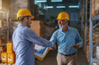 © dusanpetkovic1 - Supervisor congratulating for good results in sale. Younger man holding folder with data while older one holding tablet. Both having yellow helmets on heads. Warehouse interior.