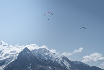 two parachouttes going side to side in the blue sky with clouds in the french alps, chamonix during 