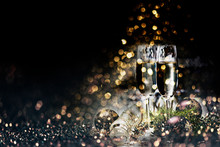 Two Champagne Glasses And Christmas Decoration Over Dark Golden Bokeh Background.