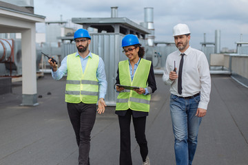 Two architects men and their assistance African woman analyzing the plan of construction site walking on the rooftop of construction holding a tablet they have a concentrated discussion.