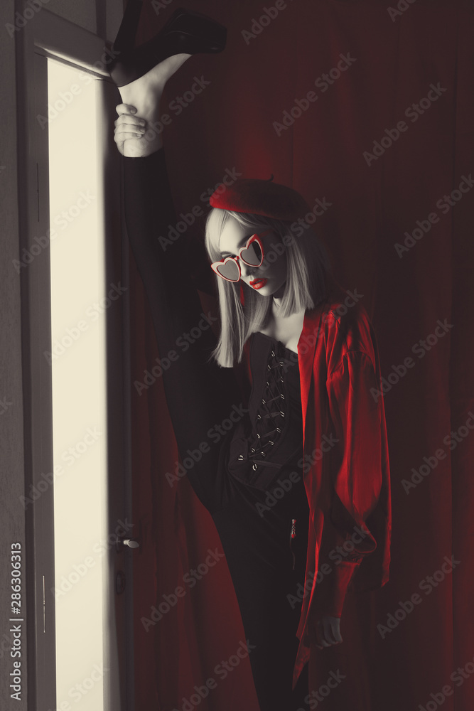 French girl in red beret with red glasses with heart and big beautiful eyes in an interior loft studio lifts her leg up in standing twine. Woman in red jacket. Fashionable female with white hair - obrazy, fototapety, plakaty 