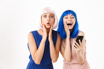 Wall Mural - Portrait of two joyful women wearing blue and pink wigs making funny face while using cellphone