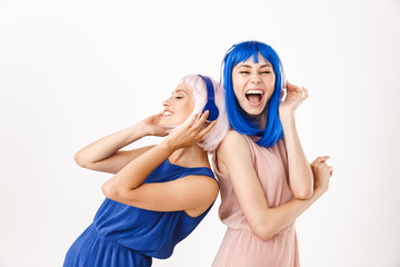 Wall Mural - Portrait of two smiling women wearing blue and pink wigs listening music with headphones