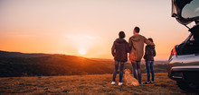 Family With Dog Embracing At Hill And Looking At Sunset