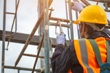Fototapeta  - [safety body construction] Working at height equipment. Fall arrestor device for worker with hooks for safety body harness on selective focus. Worker as in construction background.