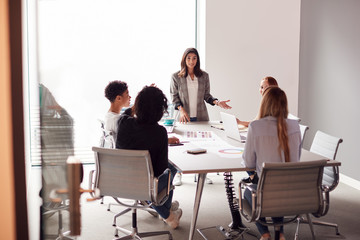 female boss gives presentation to team of young businesswomen meeting around table in modern office