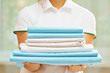 © Olga - Closeup of woman's hand holding a stack of clean folded bed sheets of blue and white colors. Blurred background.