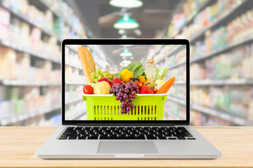 Wall Mural - supermarket aisle blurred background with laptop computer and shopping basket on wood table grocery online concept