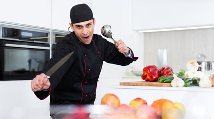 Wall Mural - Smiling male kitchener in uniform is standing with devices in the kitchen