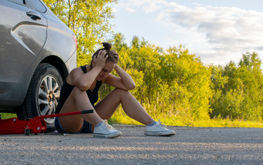 Wall Mural - A beautiful young girl tries to Jack the car to replace the wheel on the road to continue her journey.