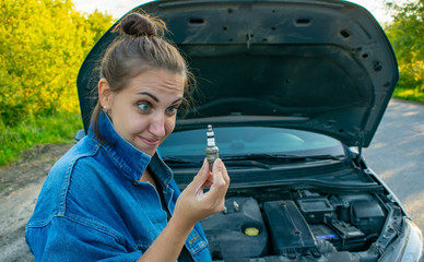 Wall Mural - A beautiful young girl tries to change the spark plugs in the car, but does not know how to do it.