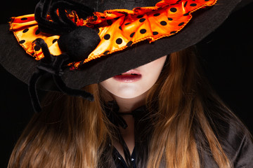 Halloween. Witch with a spider on his hat on black background. Beautiful young surprised woman in witches hat and costume holding. Wide Halloween party art design. Copy-paste. Witch craft concept