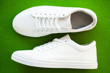 Pair of new stylish white sneakers on green background.