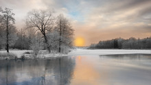 Beautiful Winter Landscape With Trees Covered In Rime Frost, And Reflection In Water Of Sunset Over River Partly Covered With Ice