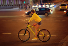 Sports Girl In Shorts Rides A Bicycle Through The City At Night. Female Is Crossing Zebra Crosswalk On Bicycle In Megapolis. Biking On The City Road