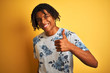© Krakenimages.com - Afro man with dreadlocks wearing summer floral t-shirt over isolated yellow background doing happy thumbs up gesture with hand. Approving expression looking at the camera with showing success.