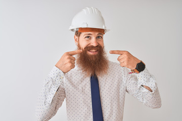 Canvas Print - Young redhead irish architect man wearing security helmet over isolated white background smiling cheerful showing and pointing with fingers teeth and mouth. Dental health concept.