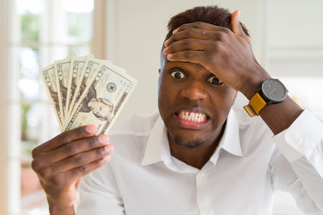 Sticker - African american man holding twenty dollars bank notes stressed with hand on head, shocked with shame and surprise face, angry and frustrated. Fear and upset for mistake.