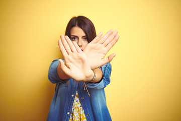 Poster - Young beautiful woman standing over yellow isolated background Rejection expression crossing arms and palms doing negative sign, angry face