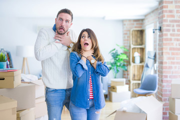 Wall Mural - Young beautiful couple standing at new home around cardboard boxes shouting and suffocate because painful strangle. Health problem. Asphyxiate and suicide concept.