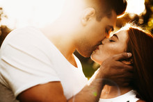 Close Up Side View Portrait Of A Beautiful Woman With Red Hair And Freckles Kissing With Her Boyfriend With Eyes Closed While Against Sunset.
