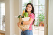 © Krakenimages.com - Beautiful young woman smiling holding a paper bag full of fresh groceries at home