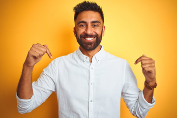 Indian businessman wearing white elegant shirt standing over isolated yellow background looking confident with smile on face, pointing oneself with fingers proud and happy.