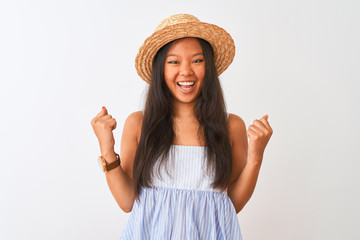 Young chinese woman wearing striped dress and hat standing over isolated white background very happy and excited doing winner gesture with arms raised, smiling and screaming for success. 