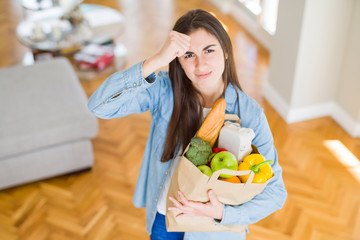 Poster - Beautiful young woman holding paper bag full of healthy groceries annoyed and frustrated shouting with anger, crazy and yelling with raised hand, anger concept