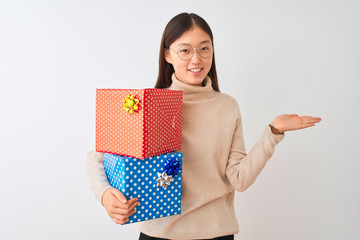 Canvas Print - Young chinese woman holding birthday gifts over isolated white background smiling cheerful presenting and pointing with palm of hand looking at the camera.