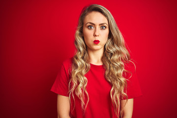 Poster - Young beautiful woman wearing basic t-shirt standing over red isolated background puffing cheeks with funny face. Mouth inflated with air, crazy expression.