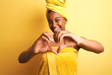 African American Woman Wearing Towel After Shower Standing Over Isolated Yellow Background Smiling In Love Showing Heart Symbol And Shape With Hands. Romantic Concept.
