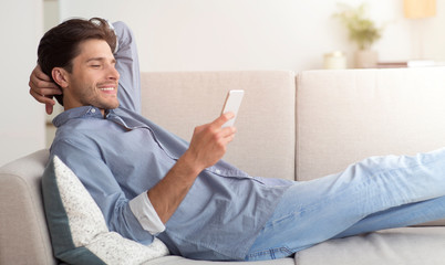 Poster - Relaxed Man Browsing On Smartphone Lying On Sofa At Home