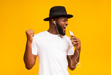 Happy African Man In Hat Singing Into Smartphone Like Microphone