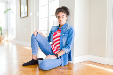 Canvas Print - Beautiful young african american woman with afro hair sitting on the floor with serious expression on face. Simple and natural looking at the camera.