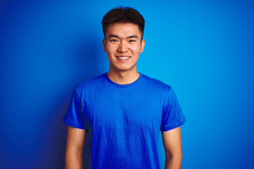 Young asian chinese man wearing t-shirt standing over isolated blue background with a happy and cool smile on face. Lucky person.