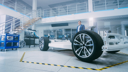 Poster - Automotive Design Engineer Looking at Electric Car Chassis Prototype. In Innovation Laboratory Facility Concept Vehicle Frame Includes Wheels, Engine and Battery.