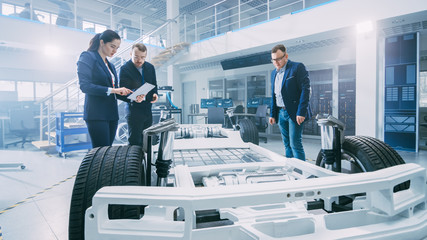 Fototapete - Automotive Design Engineers Talking while Working on Electric Car Chassis Prototype. In Innovation Laboratory Facility Concept Vehicle Frame Includes Wheels, Suspension, Engine and Battery.