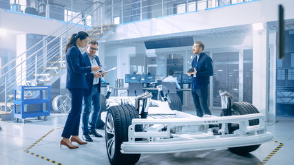 Fototapete - Automotive Design Engineers Talking while Working on Electric Car Chassis Prototype. In Innovation Laboratory Facility Concept Vehicle Frame Includes Wheels, Suspension, Engine and Battery.