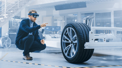Fototapete - Automotive Engineer Working on Electric Car Chassis Platform, Using Augmented Reality Headset. In Innovation Laboratory Facility Concept Vehicle Frame Includes Wheels, Suspension, Engine and Battery.
