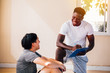 © twinsterphoto - African American fitness instructor with clipboard writing down results of exhausted sportsman sitting on floor exercising and smiling