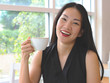 © Phuttharak - Asian woman holding cup of coffee smiling and looking to the camera.