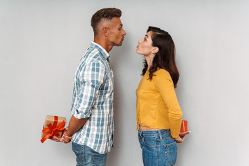 Wall Mural - Cute optimistic adult loving couple isolated over grey wall background holding gifts for each other.