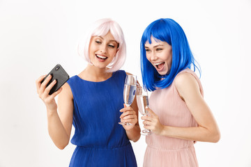 Poster - Portrait of two smiling women wearing blue and pink wigs taking selfie photo on cellphone while drinking champagne